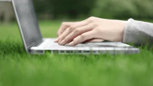 hands are working on a laptop over the green grass