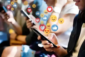Group of people using smartphones, surrounded by floating social media reaction icons, such as hearts, likes, and smiley faces, representing online engagement and interaction.