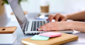 Person typing on a laptop with colorful sticky notes and a notebook on a desk, representing productivity and work environment