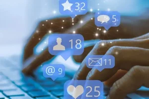 Hands typing on a laptop with floating social media icons representing likes, messages, and followers, symbolizing online engagement and activity.